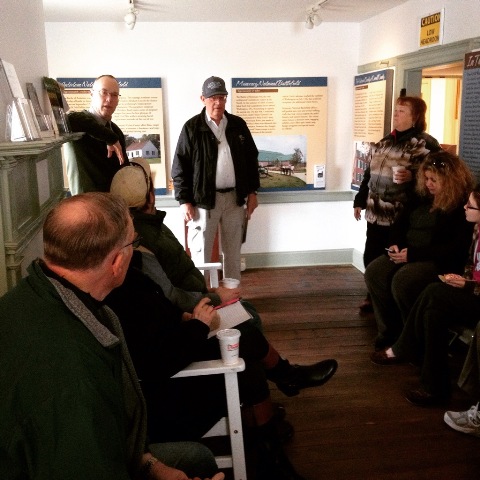 A group of volunteers sits in the historic Newcomer House listening to a park ranger speak.