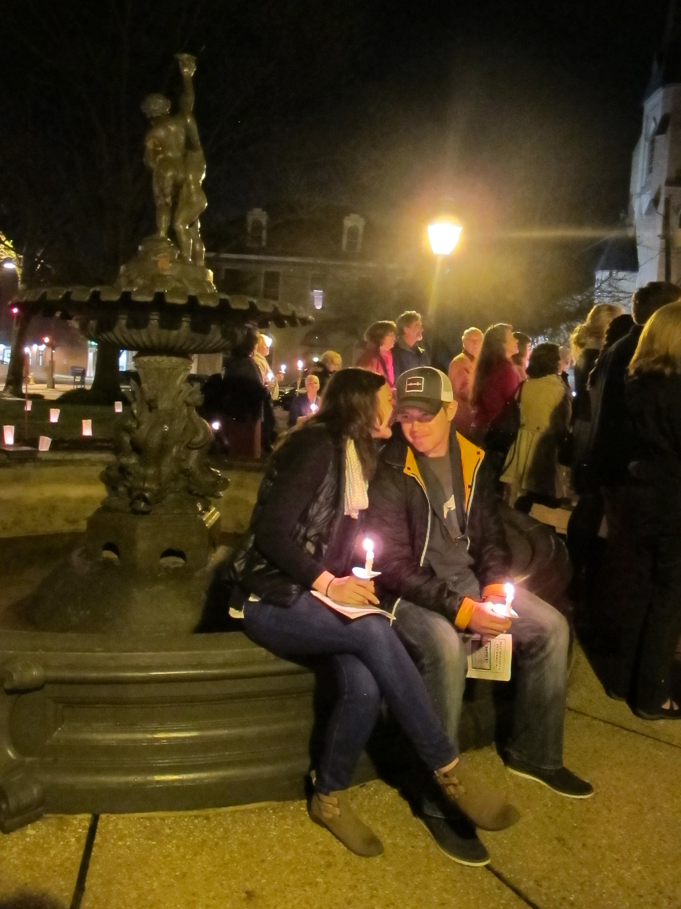 A young man and woman holding candles by the fountain at City Hall in Frederick.