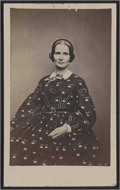 A 19th century woman poses for a black and white photo in a gown.